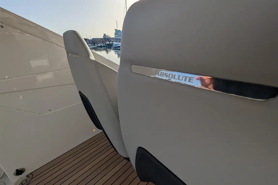 Close-up of a sleek boat seat, featuring the word "ABSOLUTE" on its chrome detail, with a marina view in the background.